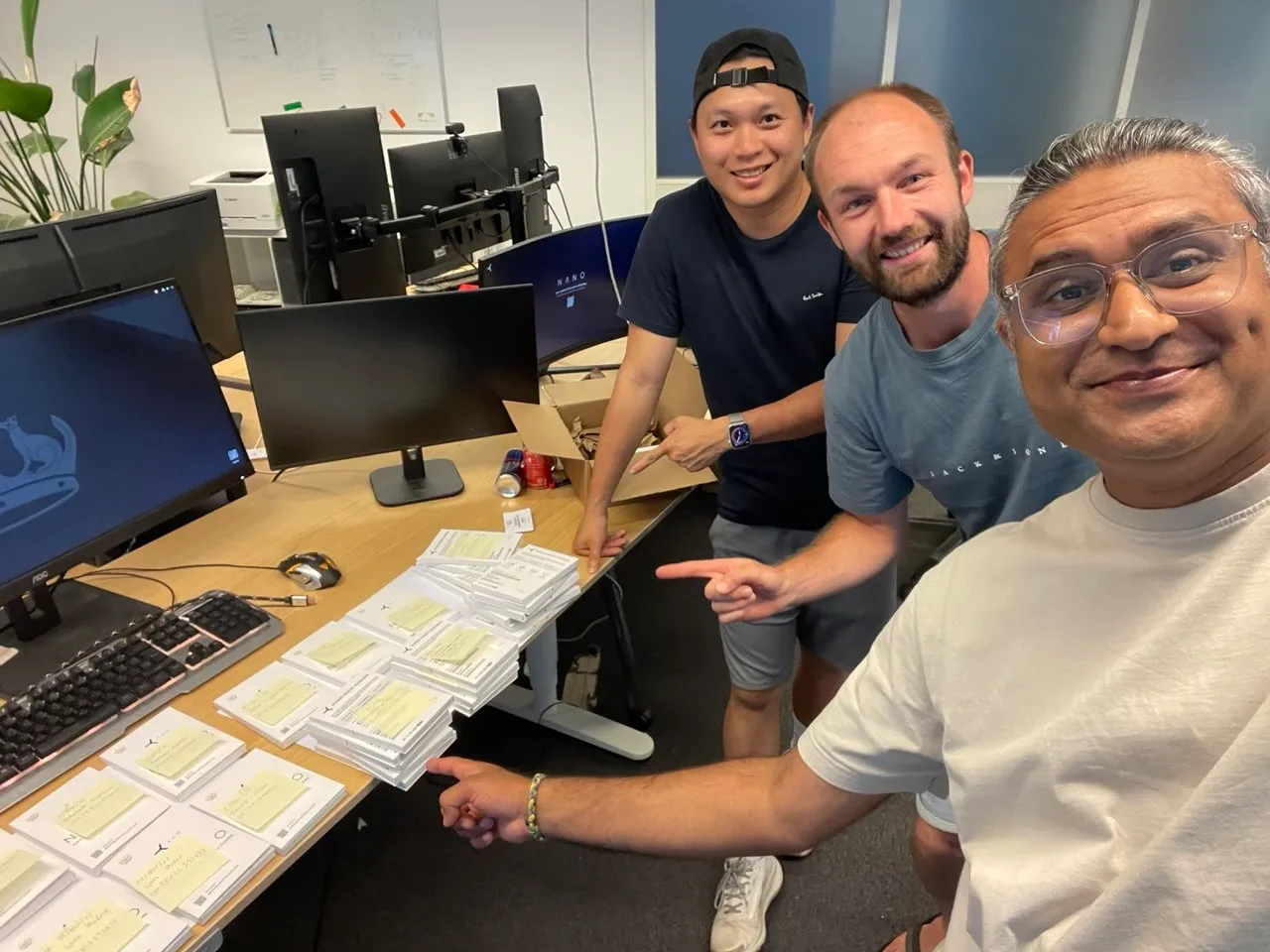 Three YOM team members at a desk in the Amsterdam office, next to stacks of printed NANO onboarding cards